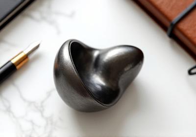 Pisapapeles escultórico de metal, con texturas sutiles y forma abstracta.